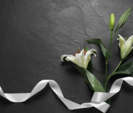White lilies and ribbon on black table, flat lay with space for text. Funeral symbols